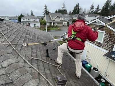 A roof cleaning contractor works on a roof, using a ladder to reach high areas for cleaning and maintenance.