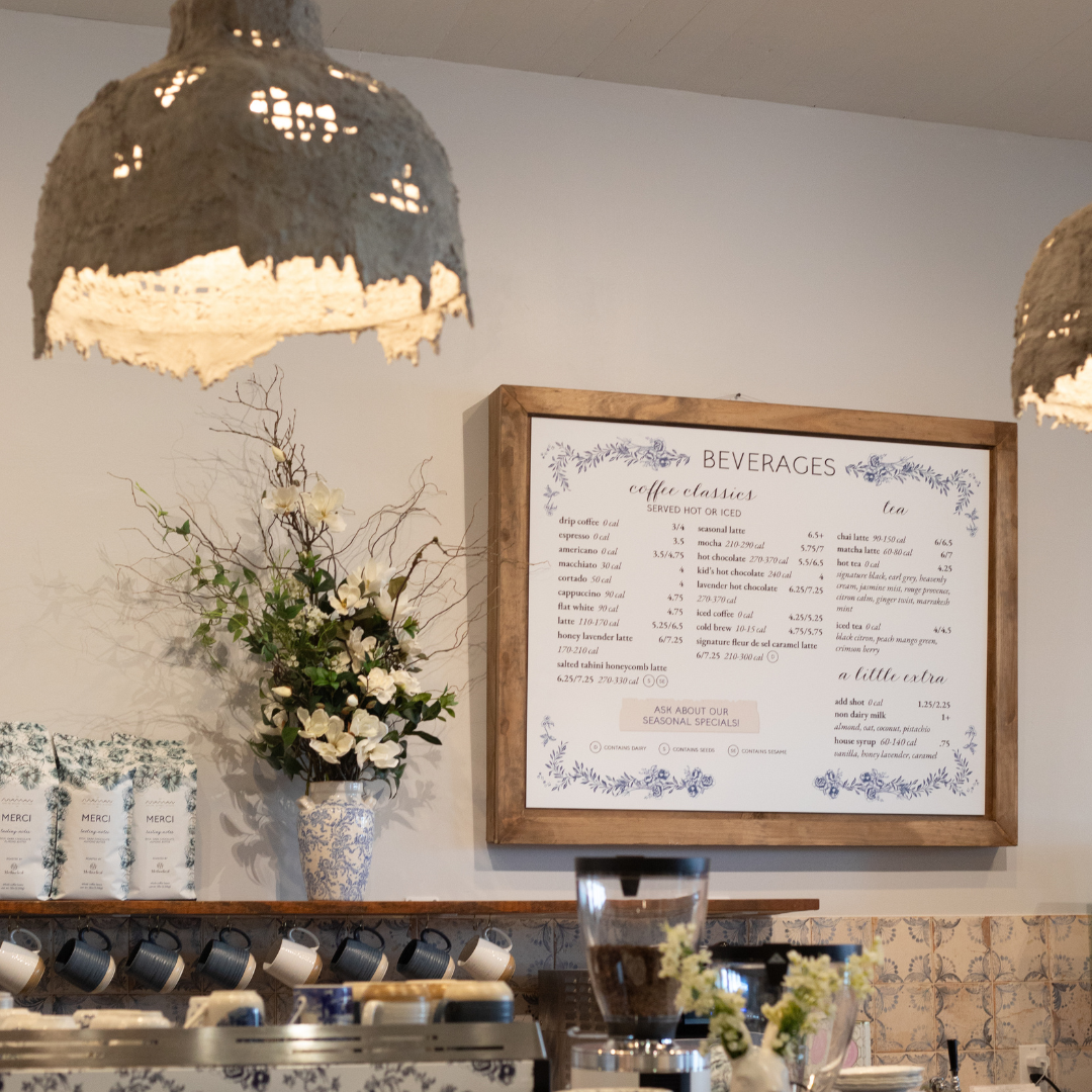 The image depicts a cozy coffee shop interior featuring a beverage menu prominently displayed on a w 
