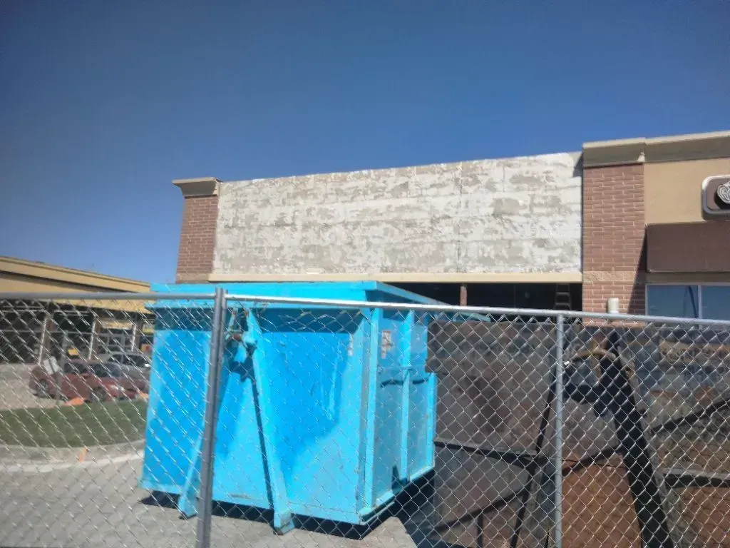Commercial building exterior under renovation with faded signage removed, construction fencing in fr 