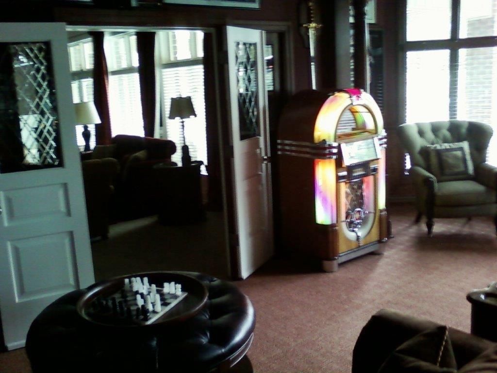 A cozy living room featuring a vintage-style jukebox, upholstered seating, and large windows. Warm lighting and classic d&eacute;cor elements create a relaxed, inviting space for entertainment and leisure activities.