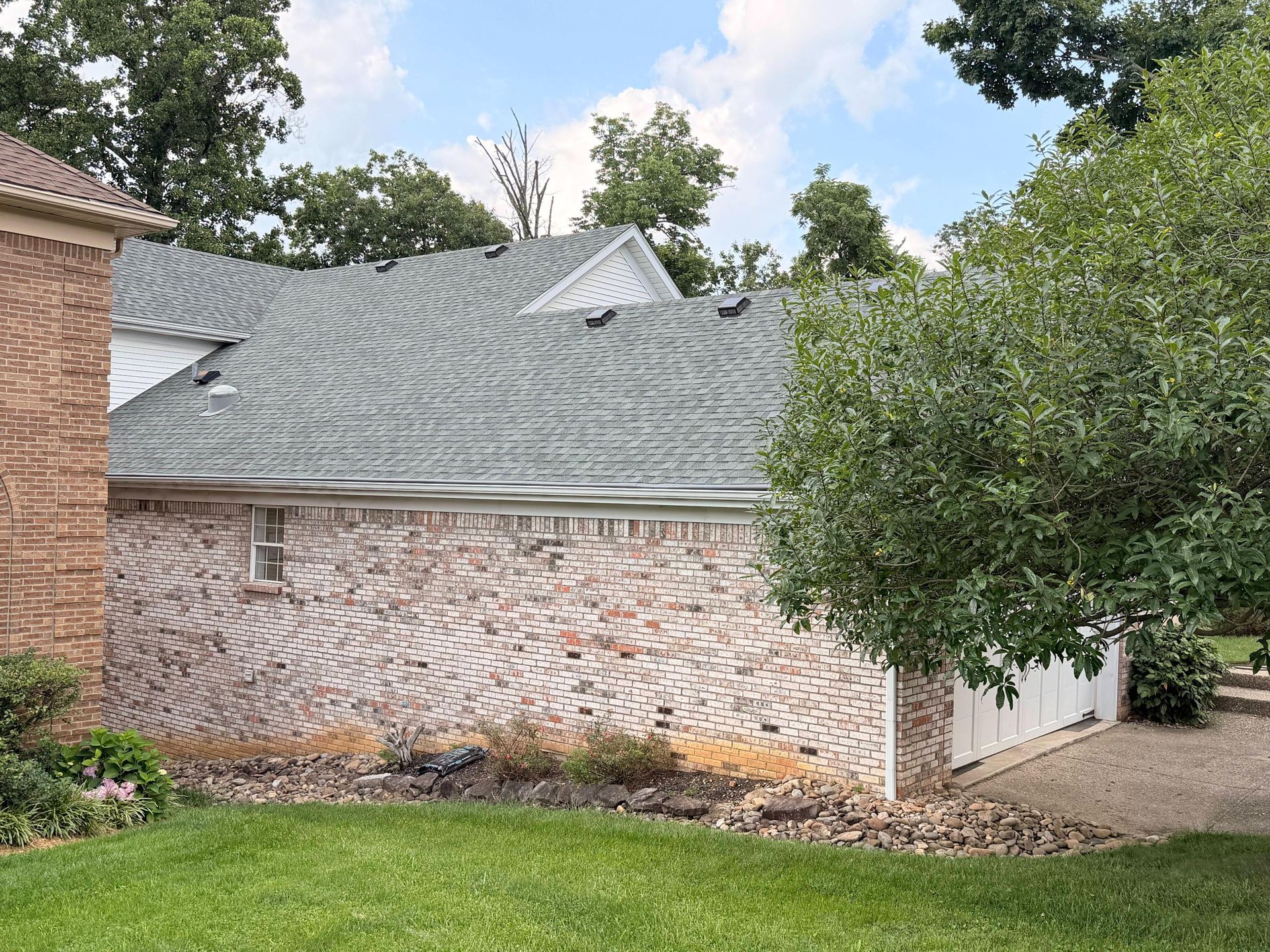 Side elevation of a residential home displaying a newly installed gray asphalt roofing system with c 