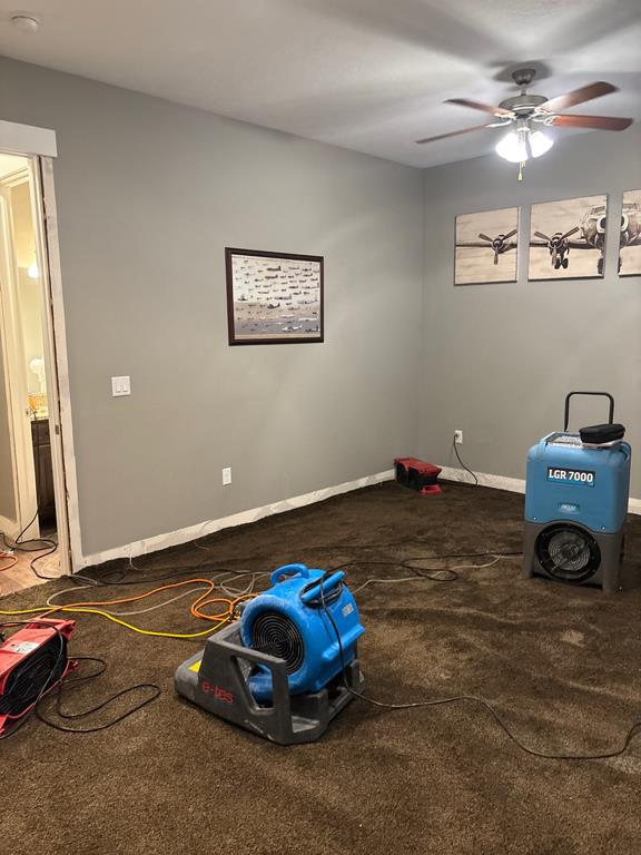 A room with brown carpet is set up with equipment for drying and air circulation. Two industrial fan 