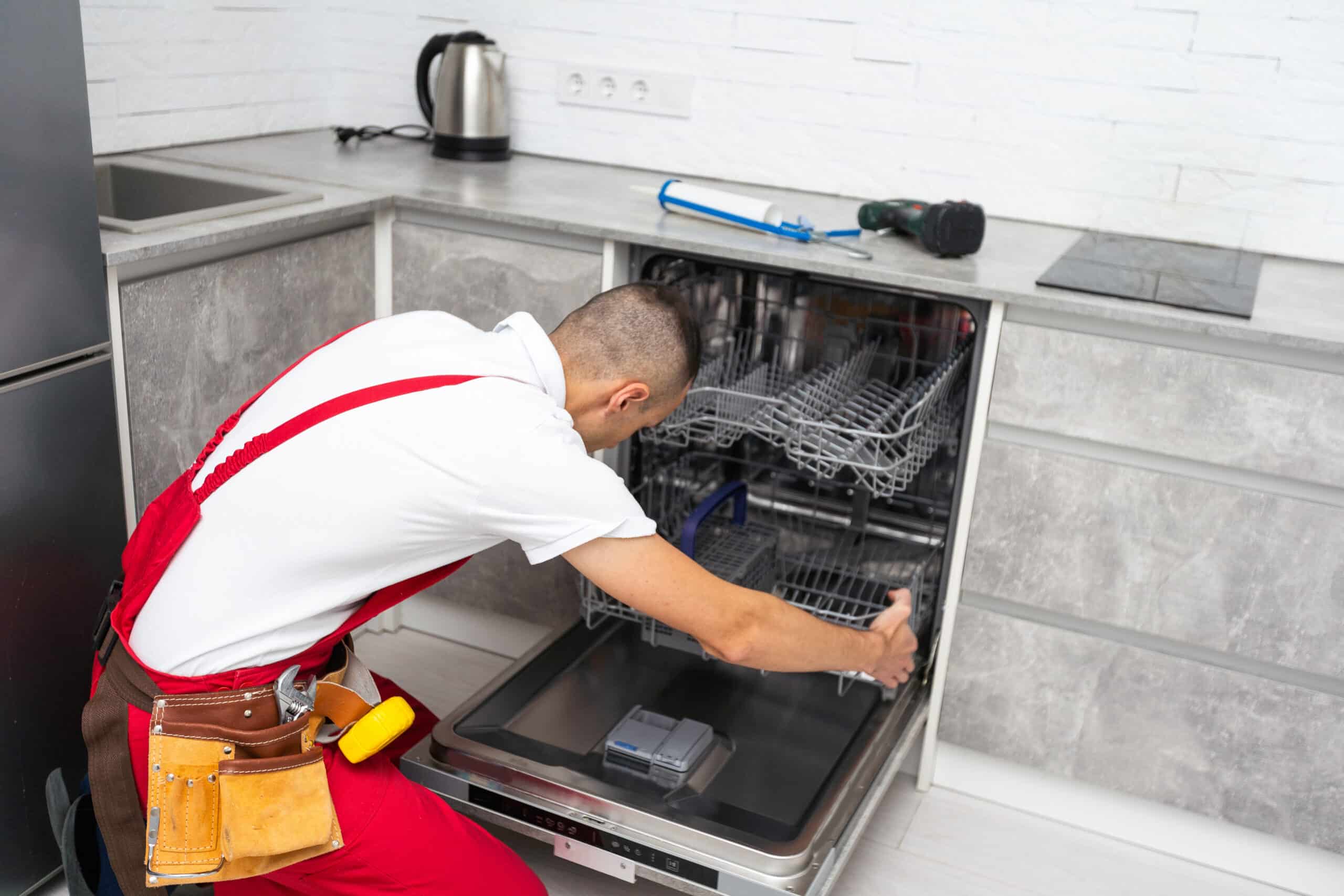 The dishwasher open with a man who is putting the bottom tray back into it