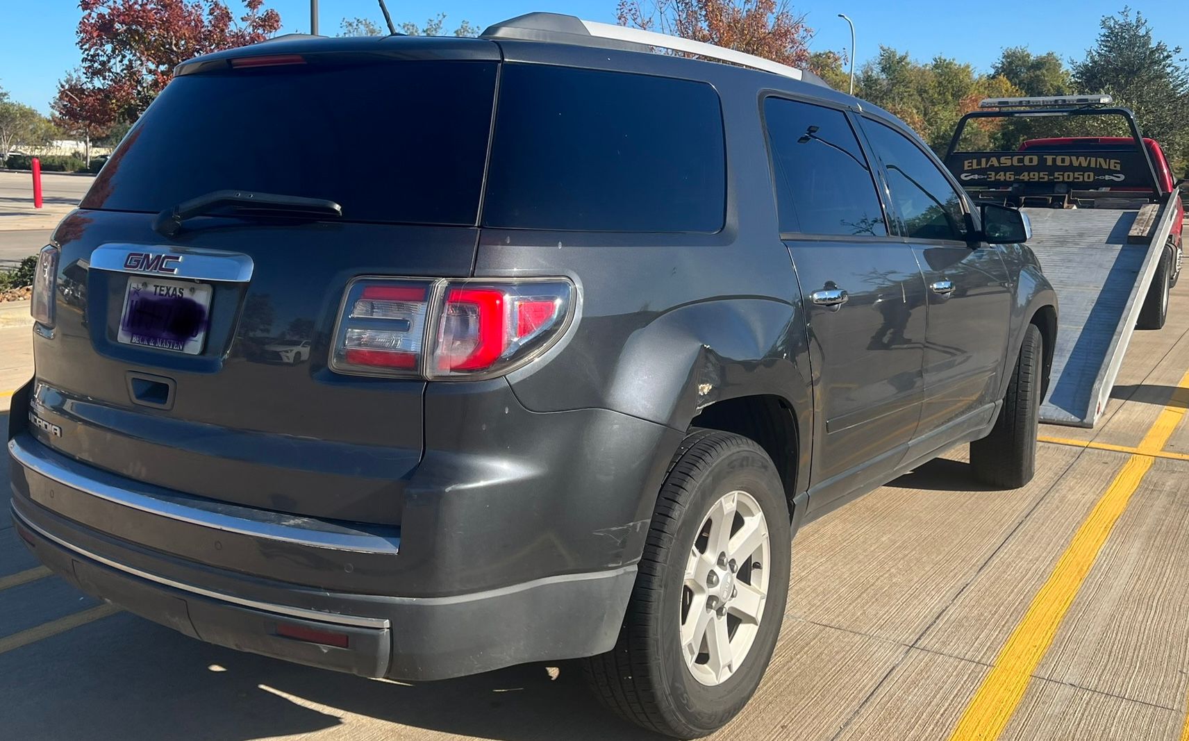 A dark gray GMC Yukon is transported on an Eliasco Towing flatbed truck along a roadway, highlighting professional vehicle towing and safe transportation services during daylight hours.