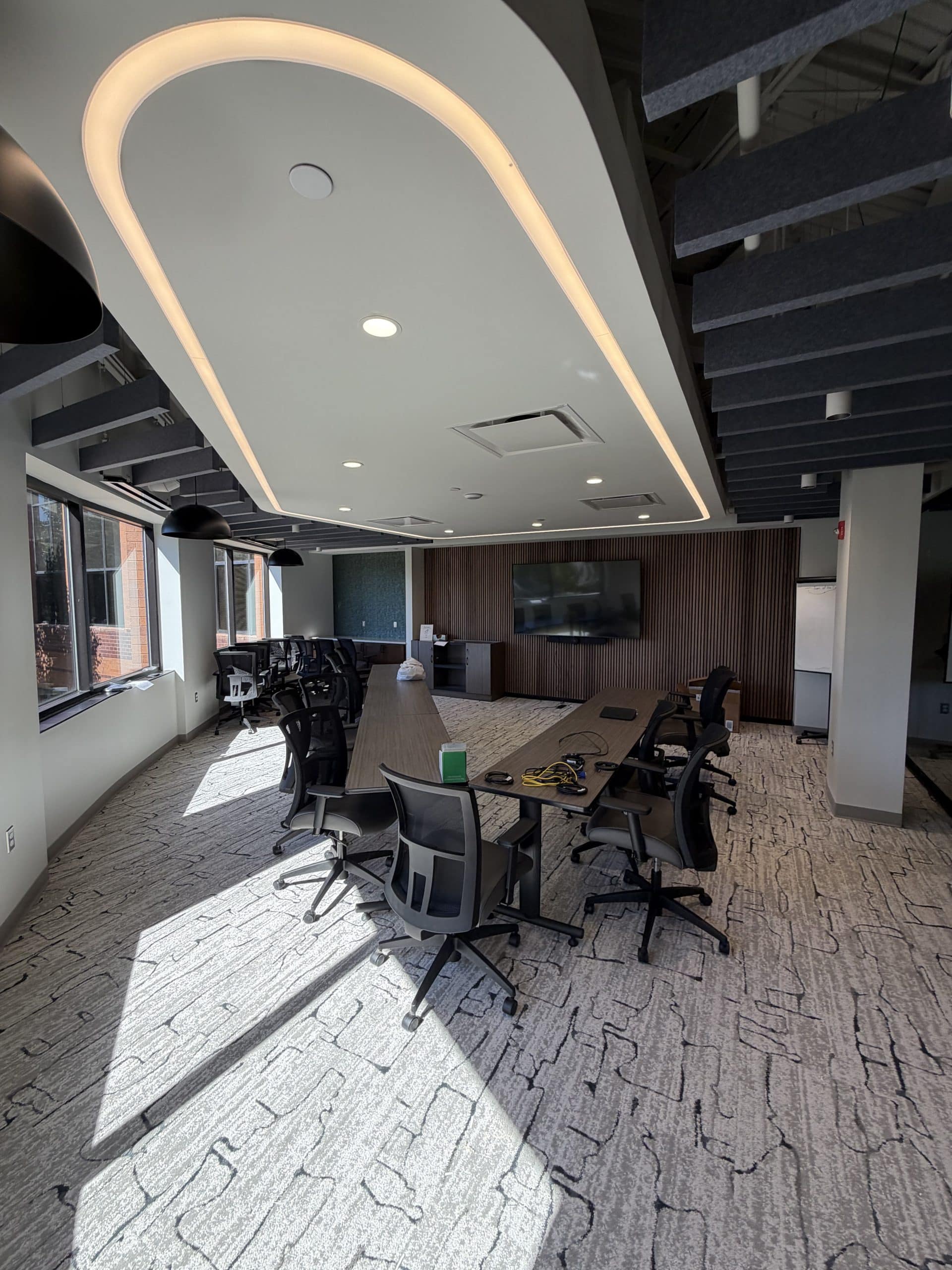 A modern meeting space at the Toll Brothers Michigan Division Office & Design Studio showcases the interior detail of this Schonsheck, Inc. commercial construction project. Natural light, distinctive ceiling lighting, and a wood slat accent wall create a welcoming setting for collaboration. The space reflects the balance of functionality and visual appeal that businesses seek in professional office interiors.