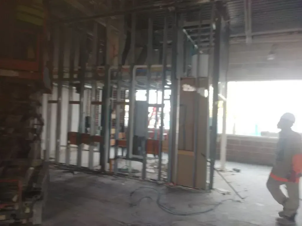 Commercial interior under demolition with exposed metal framing, pipes, and wiring, debris scattered 