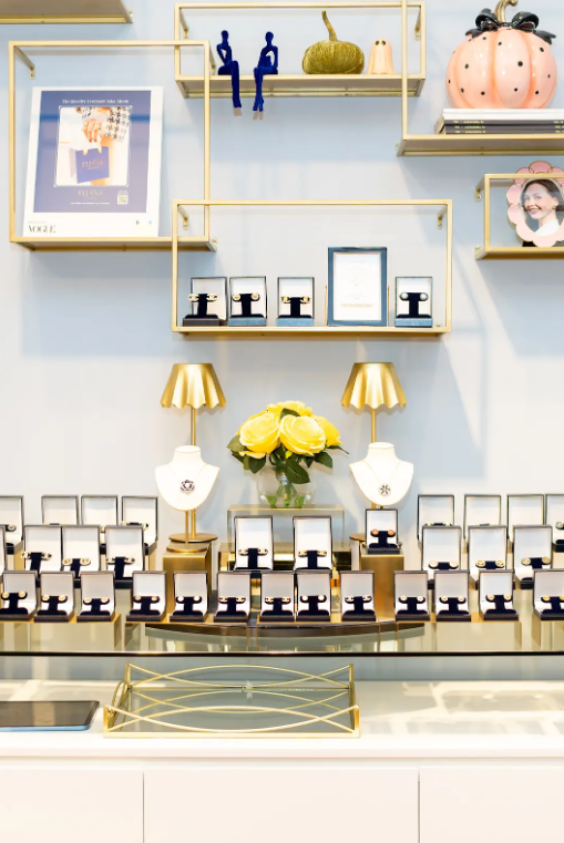 Eliana Curated showcases earrings and necklaces in decorative display boxes, accented by yellow roses, gold-tone shelves, and seasonal decor. Explore jewelry shopping in Old Town Alexandria, Virginia.