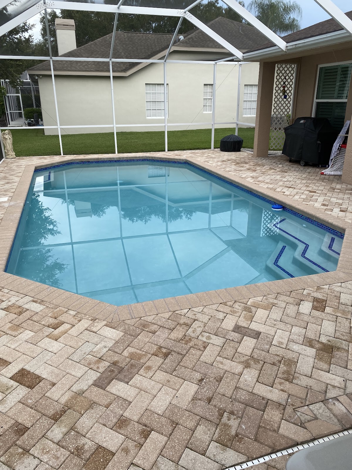 Screen-enclosed residential swimming pool with clear blue water, built-in steps, and brick paver decking.