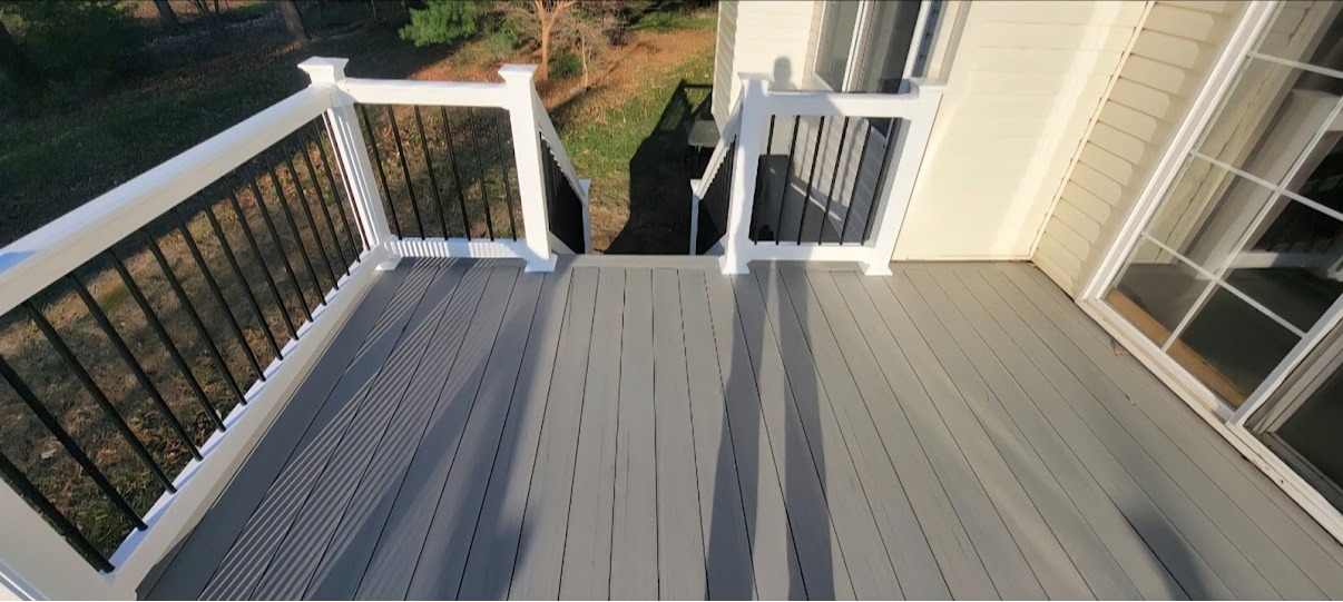 Finished residential deck featuring gray decking, white railings, black balusters, and stair access. 