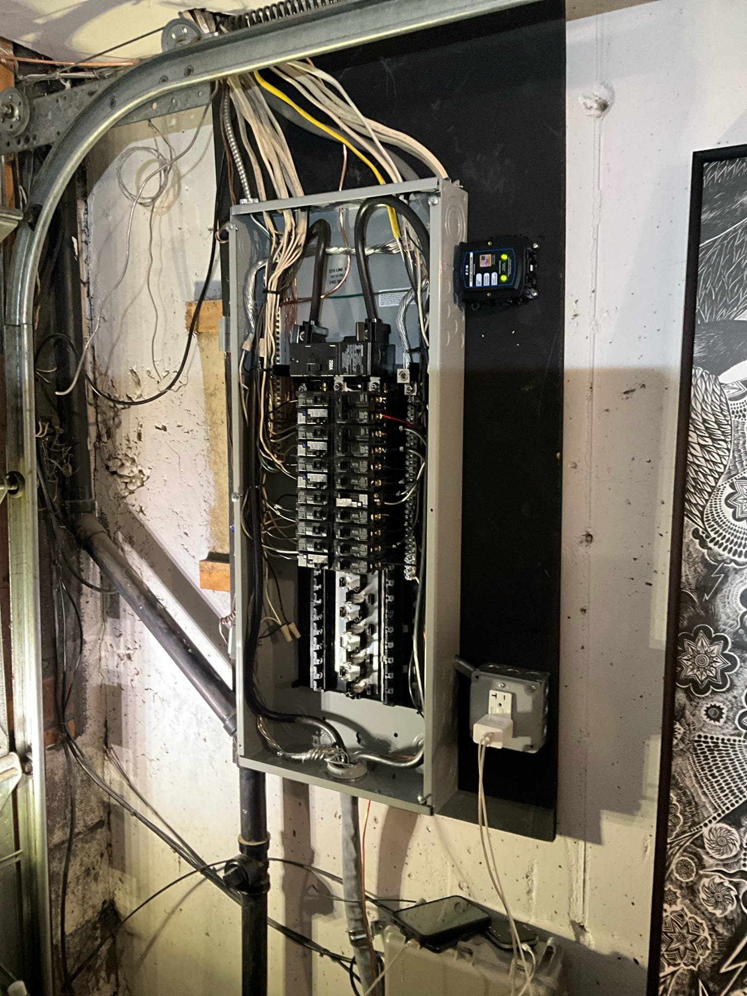 Thomas Edison Electric upgraded this breaker panel in a Philadelphia, PA basement near Cottman Ave. A surge protector is mounted alongside the enclosure, and a GFCI outlet below the panel provides code-compliant power in the utility area.