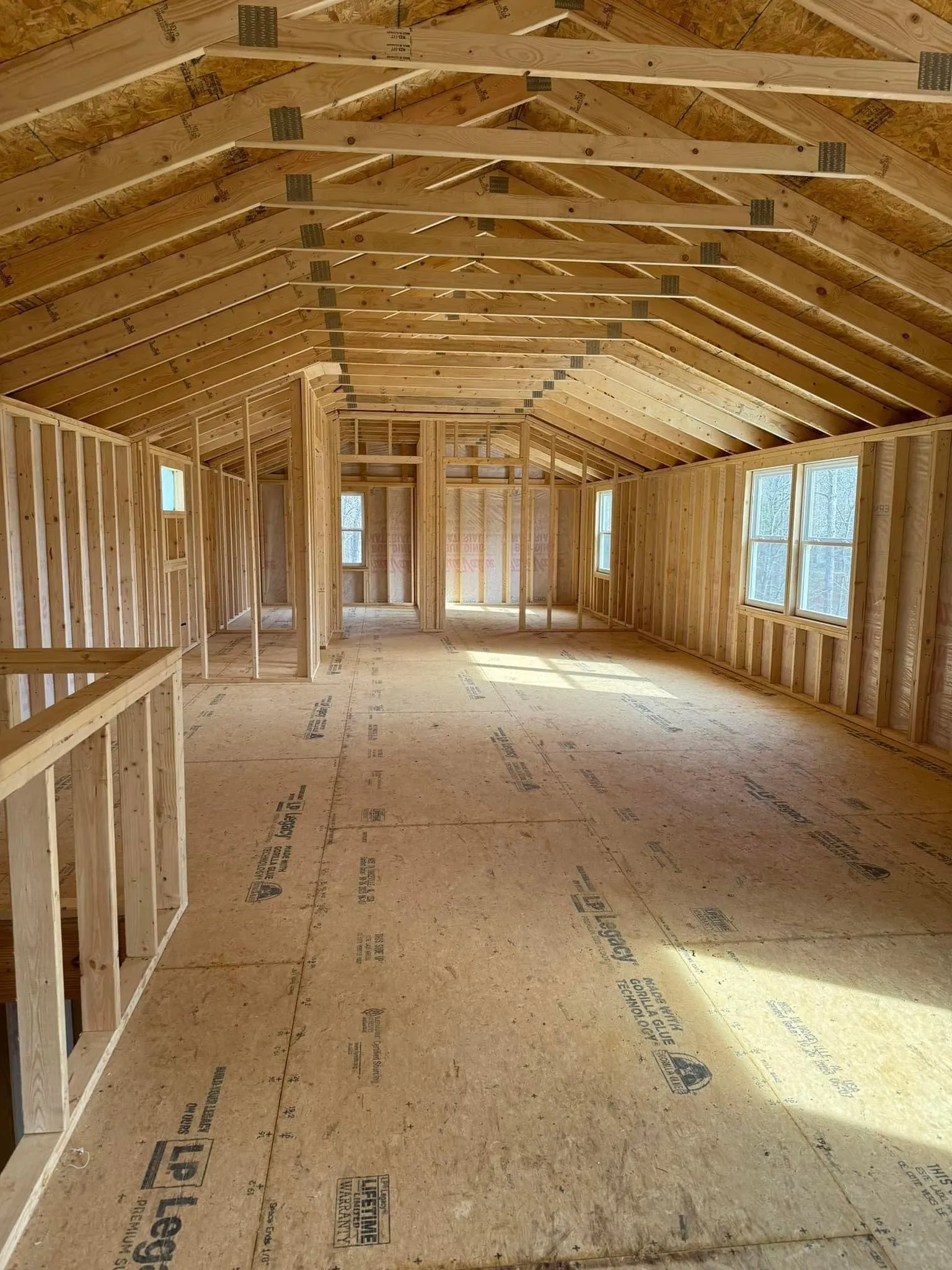 Spacious portable building interior showcasing exposed wood framing, engineered roof trusses, subflooring, and framed room layouts. Demonstrates structural quality before insulation, drywall, and finishing installation.