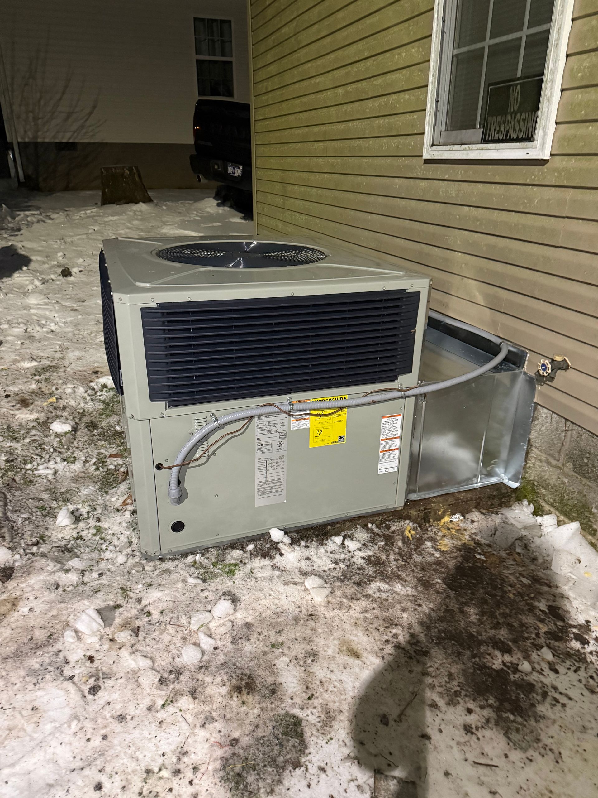 Outdoor packaged HVAC unit installed beside a residential building during winter, featuring side ven 