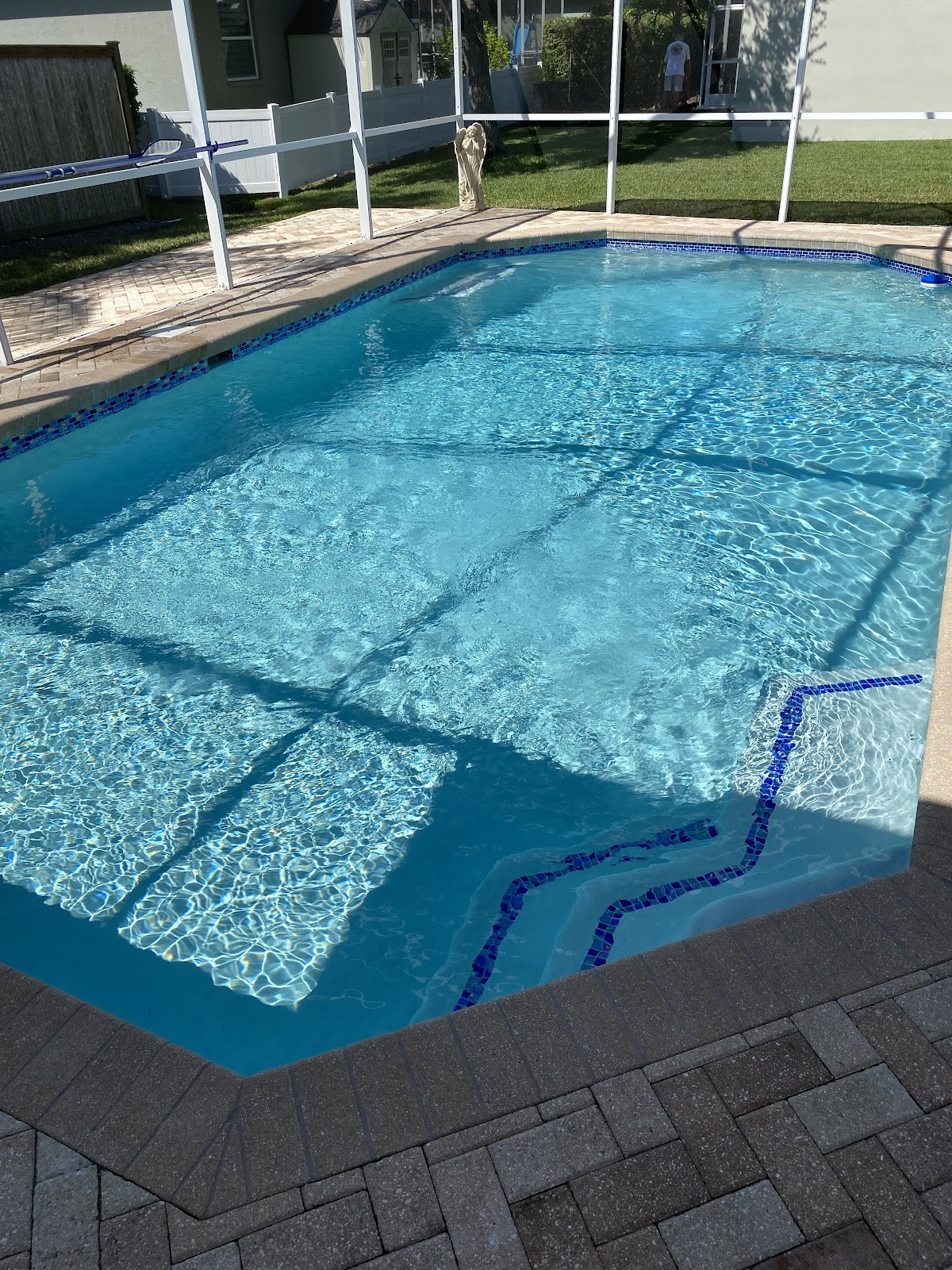 Screen-enclosed backyard swimming pool with sparkling blue water, built-in steps, and brick paver decking.