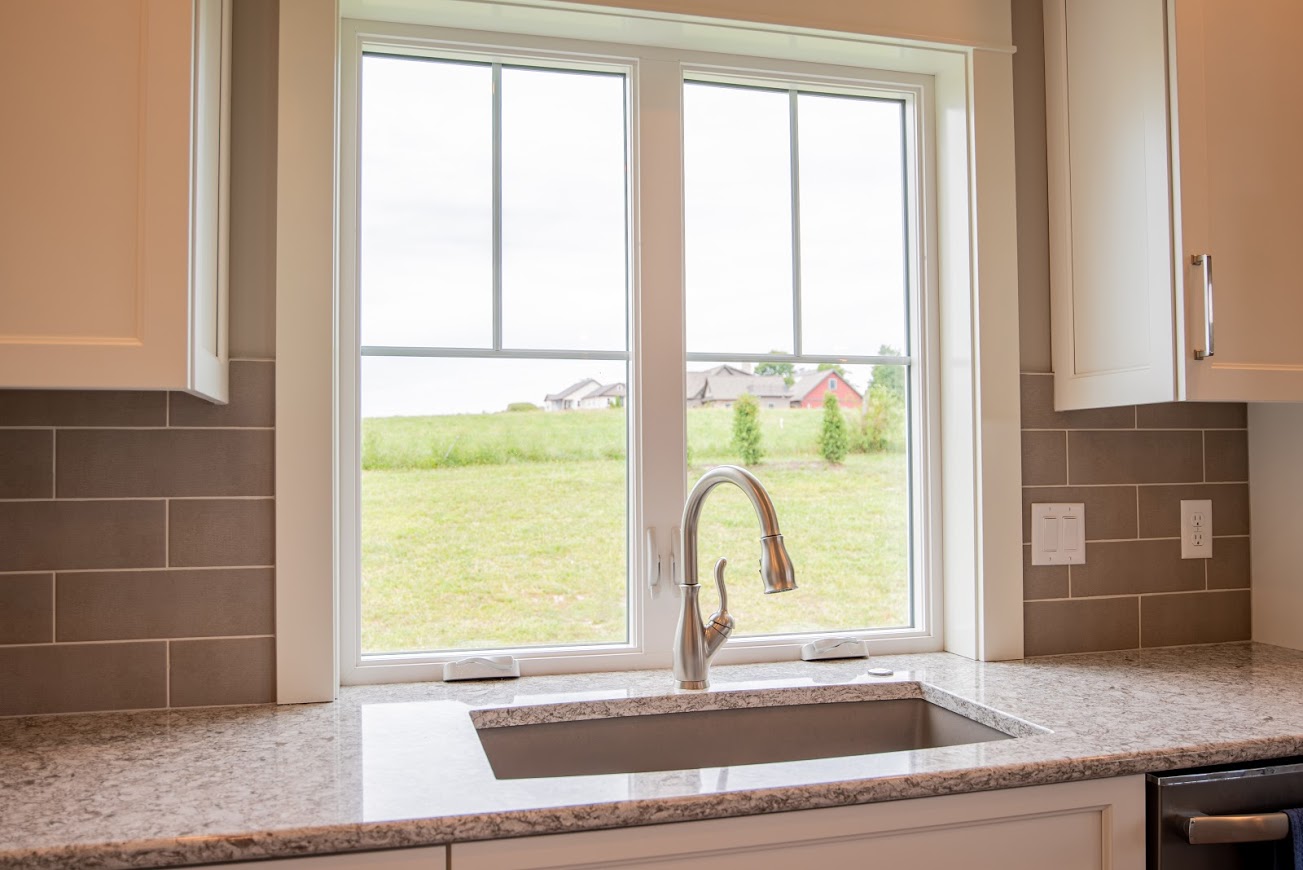 The EcoTek 3200 Series Casement Windows in this kitchen bring in natural light and offer a clear outdoor view, perfectly complementing the modern design with white cabinetry and granite countertops. These windows enhance the room's bright and airy feel while seamlessly connecting the interior and the outdoor landscape.