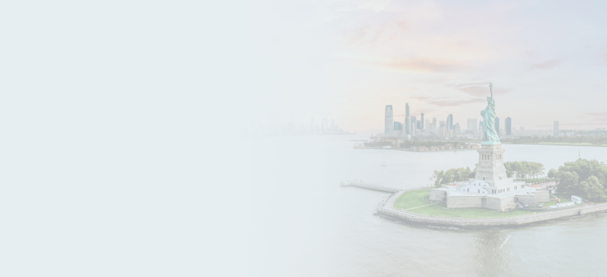 The Statue of Liberty in the foreground with New York Harbour and the city skyline in the background at sunset.