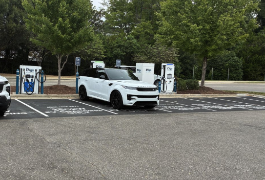 Several EVgo fast charging units installed in marked parking spaces at a public charging station, with EVgo logos on the chargers, protective bollards around each unit.