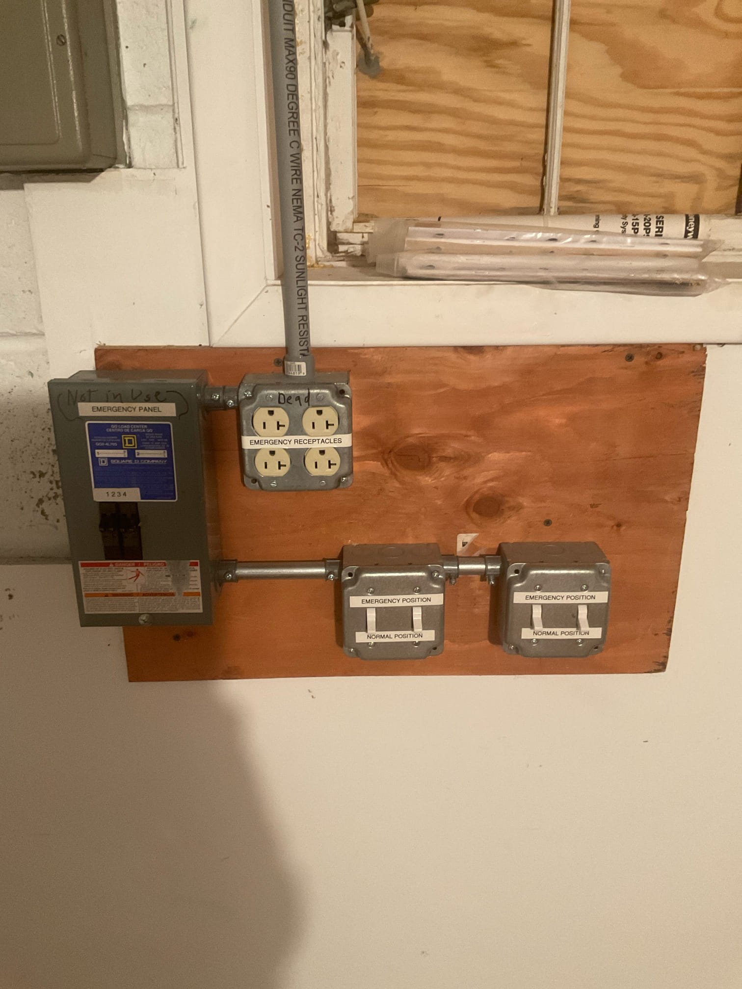 Thomas Edison Electric installed a Square D emergency panel with emergency receptacles and transfer switches at a Jenkintown, PA property. The setup includes a quad outlet for emergency power and two manual transfer position switches, all mounted on a plywood backer with rigid conduit.