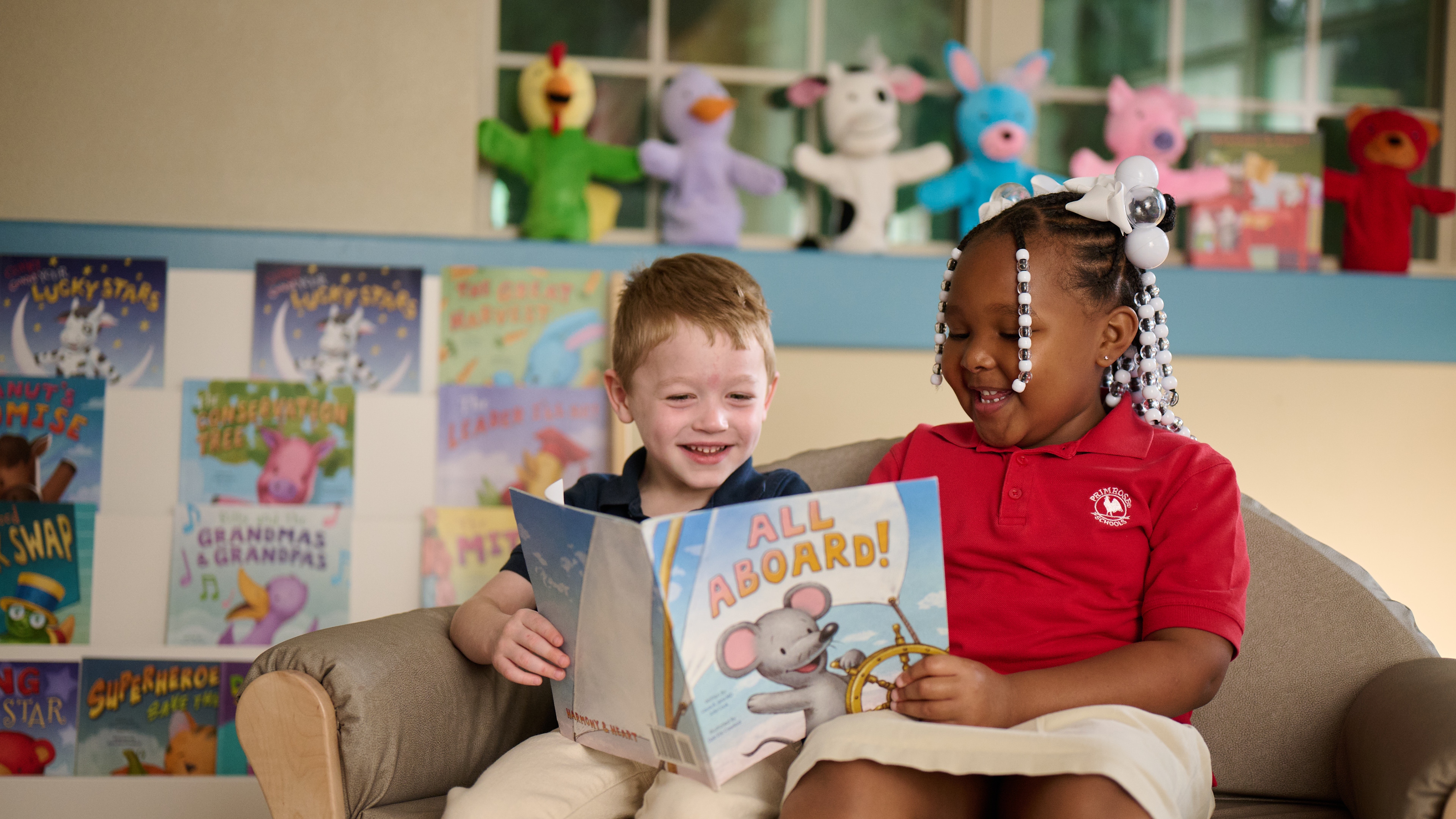 Two Primrose Schools preschool children reading All Aboard picture book together in cozy classroom library