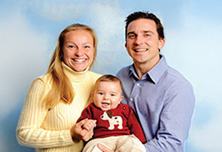 Peter Partridge smiling alongside his wife, Poppy, and infant son, Chase.