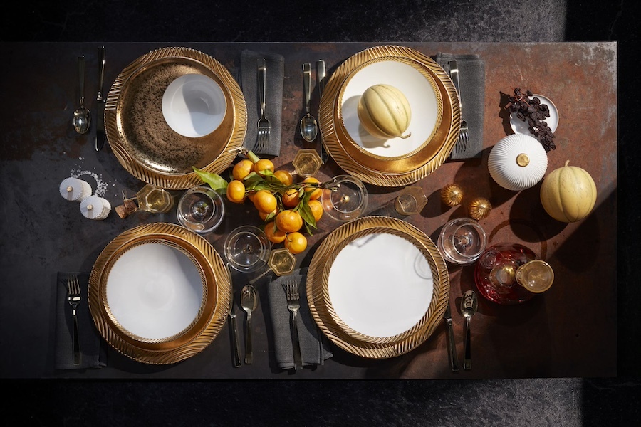 A premium product image by Tabula Rasa Social Stationers, displaying a meticulously arranged dining table with exquisite L'Objet luxury tableware. The setup highlights gold-toned, textured charger plates, pristine white dinnerware, coordinated gold cutlery, and sophisticated glassware. Adorned with decorative gourds, fresh citrus branches, and berries, this setting exudes an elegant, autumnal ambiance perfect for refined dining or seasonal entertaining.