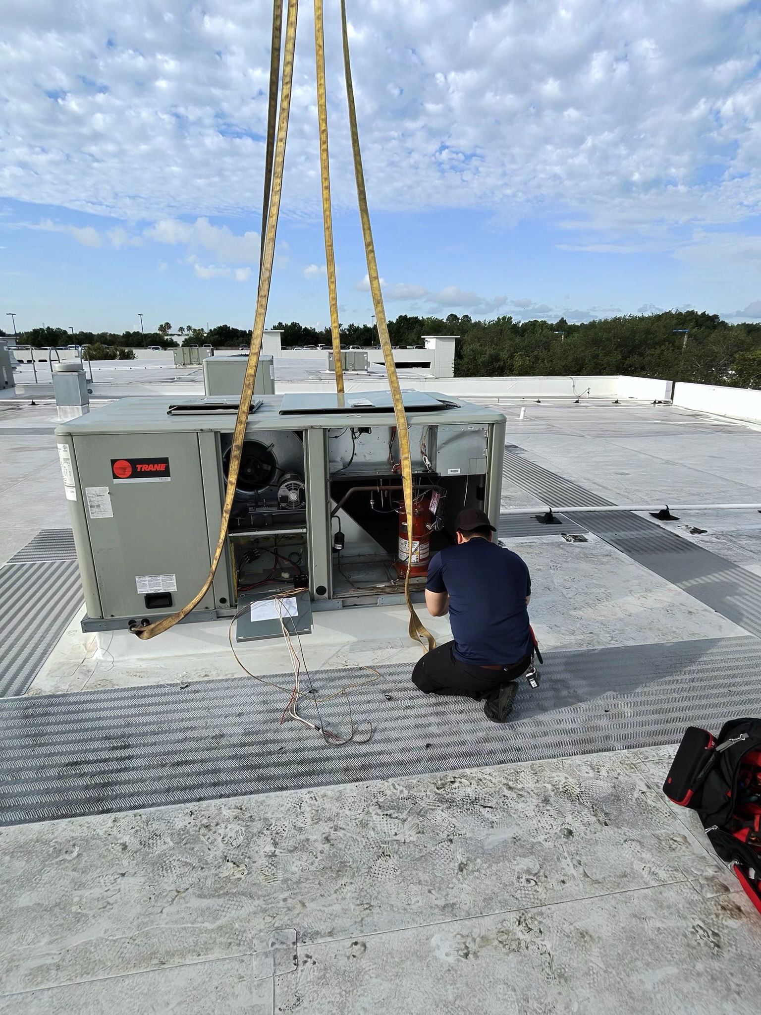 HVAC technician guiding a commercial rooftop unit into position during a crane-assisted installation 