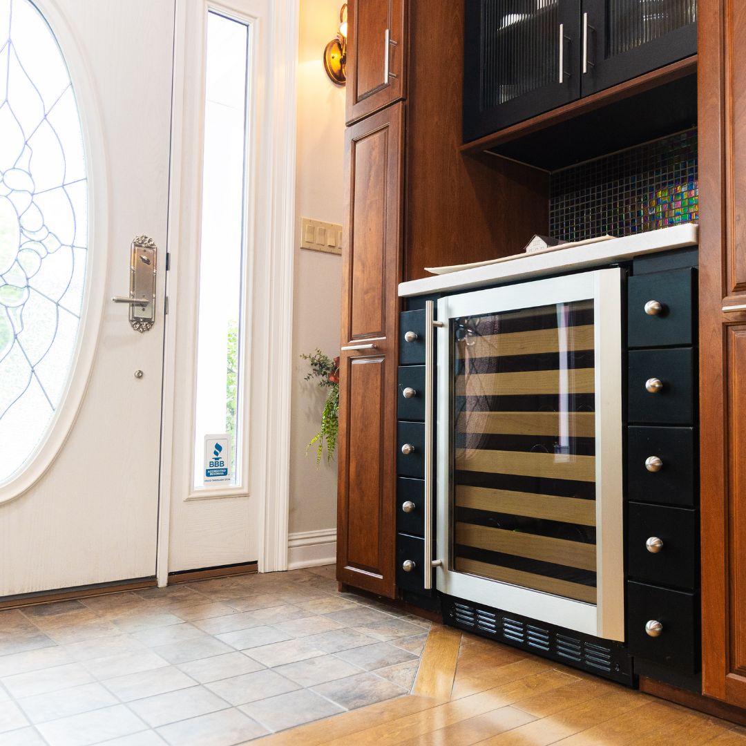 Custom cabinetry and wine fridge beside an elegant glass entry door installed by Fiderio.