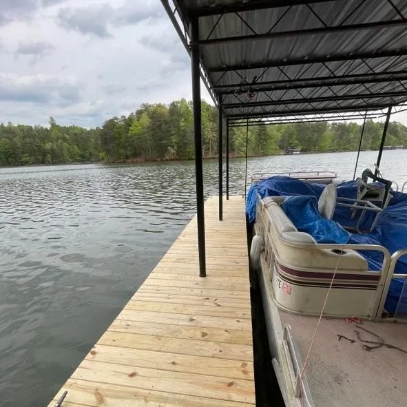 Wooden dock with covered boat slip on calm lake with trees.