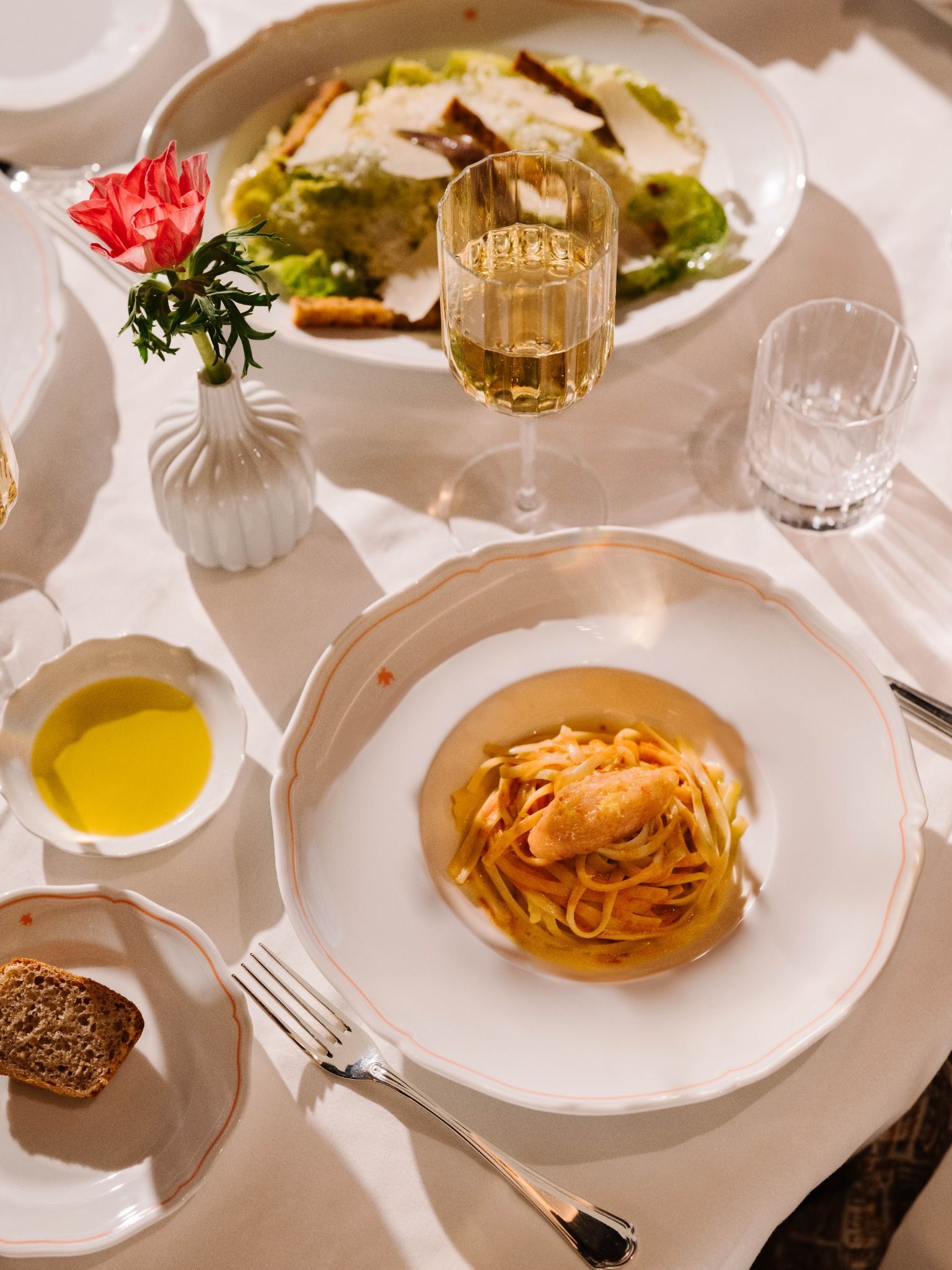 Top view of a plated pasta dish with white wine, olive oil, bread, and an elegant table setting.