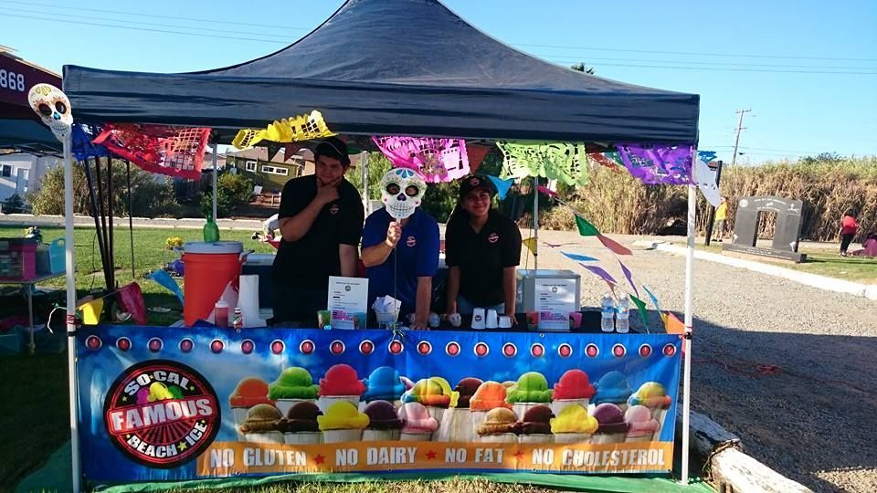 Outdoor vendor booth for So Cal Famous Beach Ice featuring colorful decorations and a branded table display. Staff members stand behind the counter serving shaved ice treats, creating a lively, festive atmosphere ideal for events, fairs, and community gatherings.