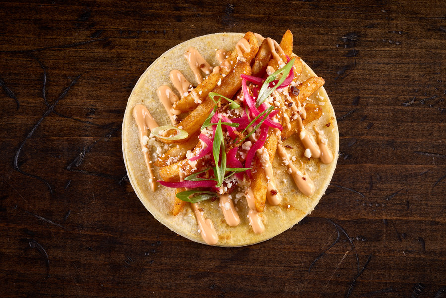 Taco with fries, barbacoa jus, spicy mayo, pickled red onion, cotija cheese, bacon