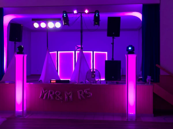 GPM Entertainment - DJ Münster DJ Münster Hochzeit auf Bühne mit pinker Beleuchtung, LED-Säulen und professioneller Soundanlage – modernes Setup für Feier mit Tanzgarantie.
