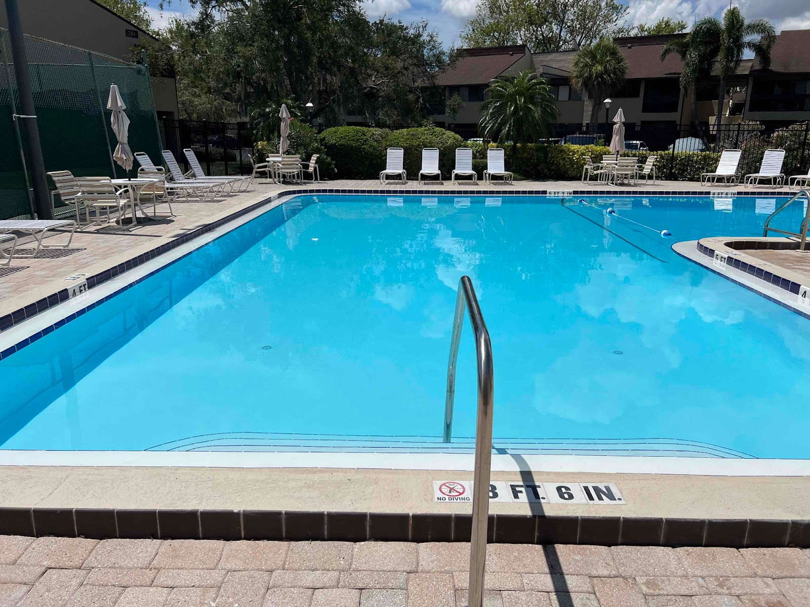 Large rectangular community swimming pool with bright blue water, entry handrails, and a spacious surrounding pool deck.