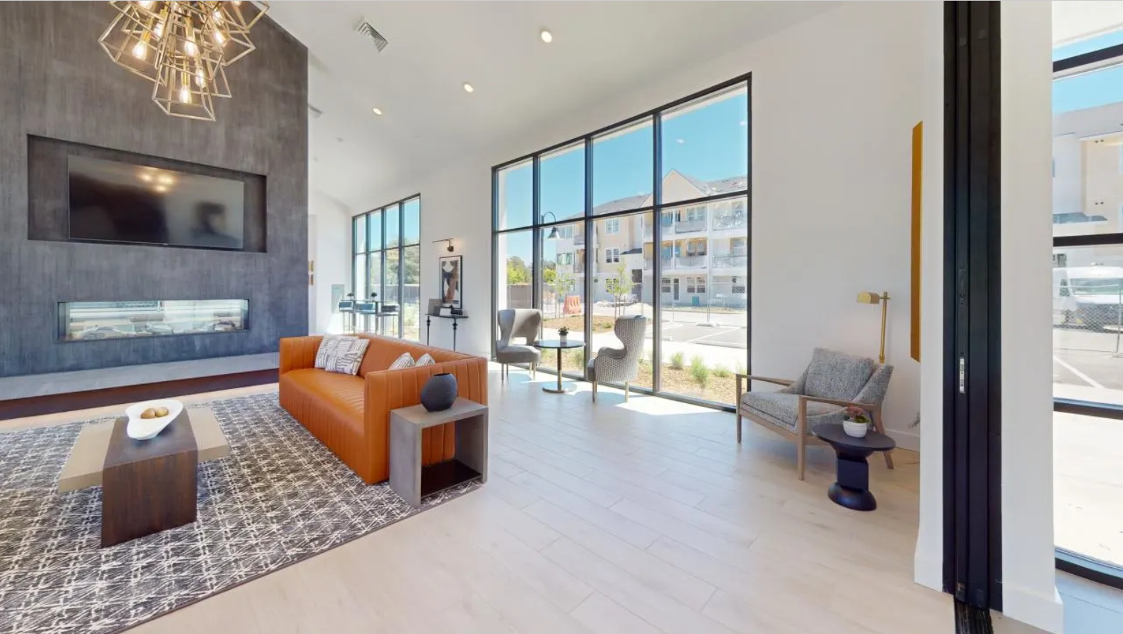 The open, spacious resident lounge with an orange couch, coffee table, and large windows