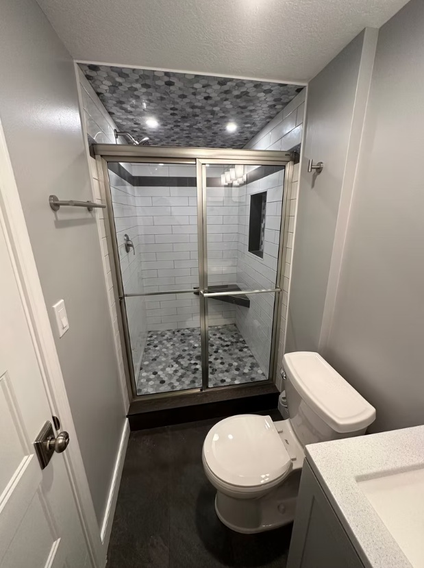 Contemporary design meets everyday luxury in this bathroom design. The standout feature is the continuous marble hexagon tile on the ceiling, which creates a real “wow” moment the second you walk in. Bright subway tile keeps the space feeling clean and classic, while dark accent bands add just the right amount of contrast for a bold, modern touch. Functional details like a built-in shower niche and a floating bench make the space as practical as it is stylish. Overall, it’s a full transformation that shows even smaller bathrooms can deliver serious design impact.Let’s chat and make it happen.