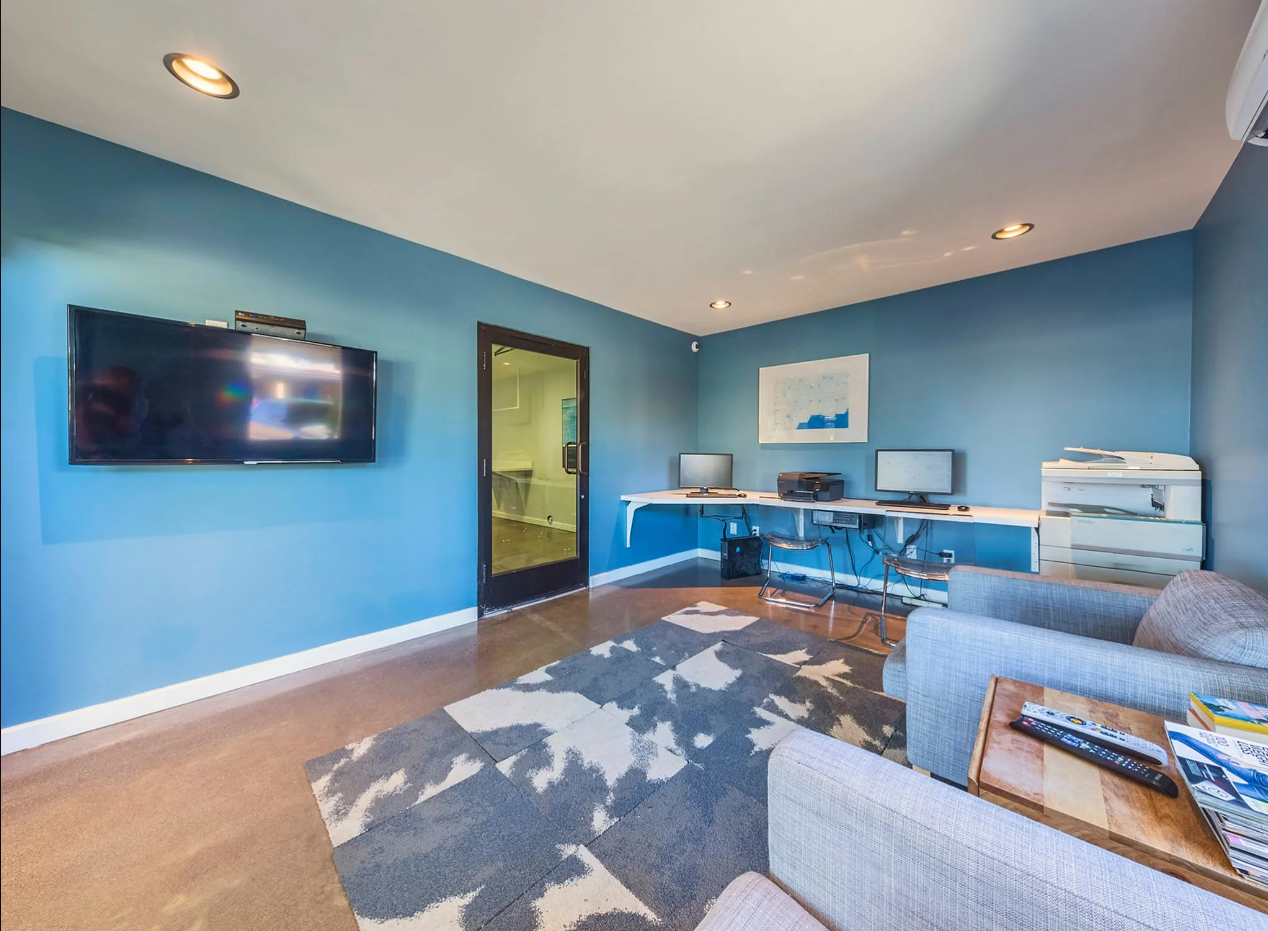 Media Room with Blue Walls and Large Television with a Desk with Computers Across the Room