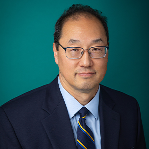 Male cardiologist smiling in front of blue photo backdrop.