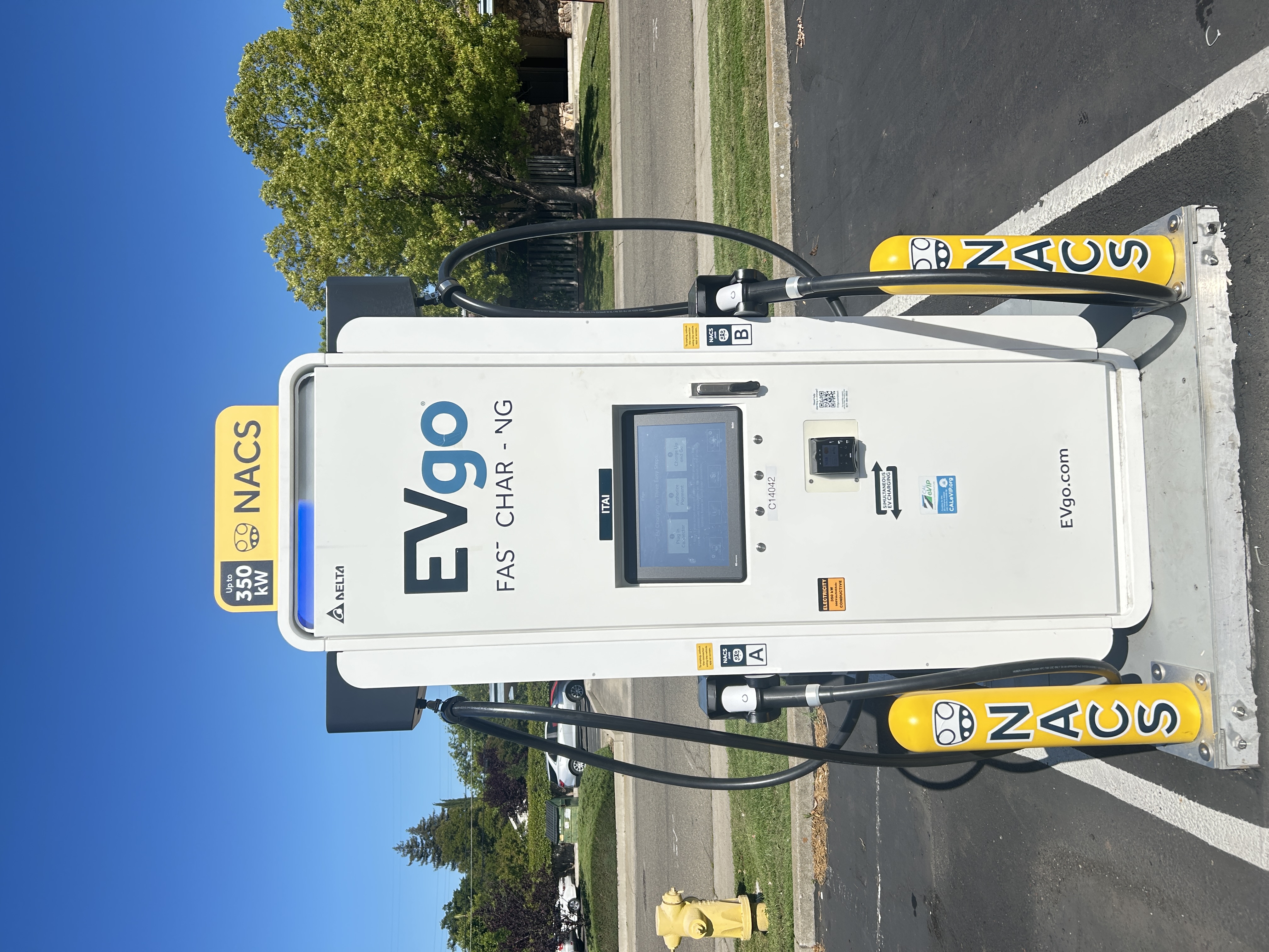 NACS EVgo fast charging unit installed in marked parking space at a public charging station, with EVgo logos on the charger,  and yellow protective bollards around the unit