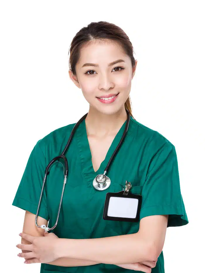 A young Asian woman wearing green medical scrubs and a stethoscope is smiling at the camera. She has her arms crossed and a name tag is attached to her scrubs. The background is white.