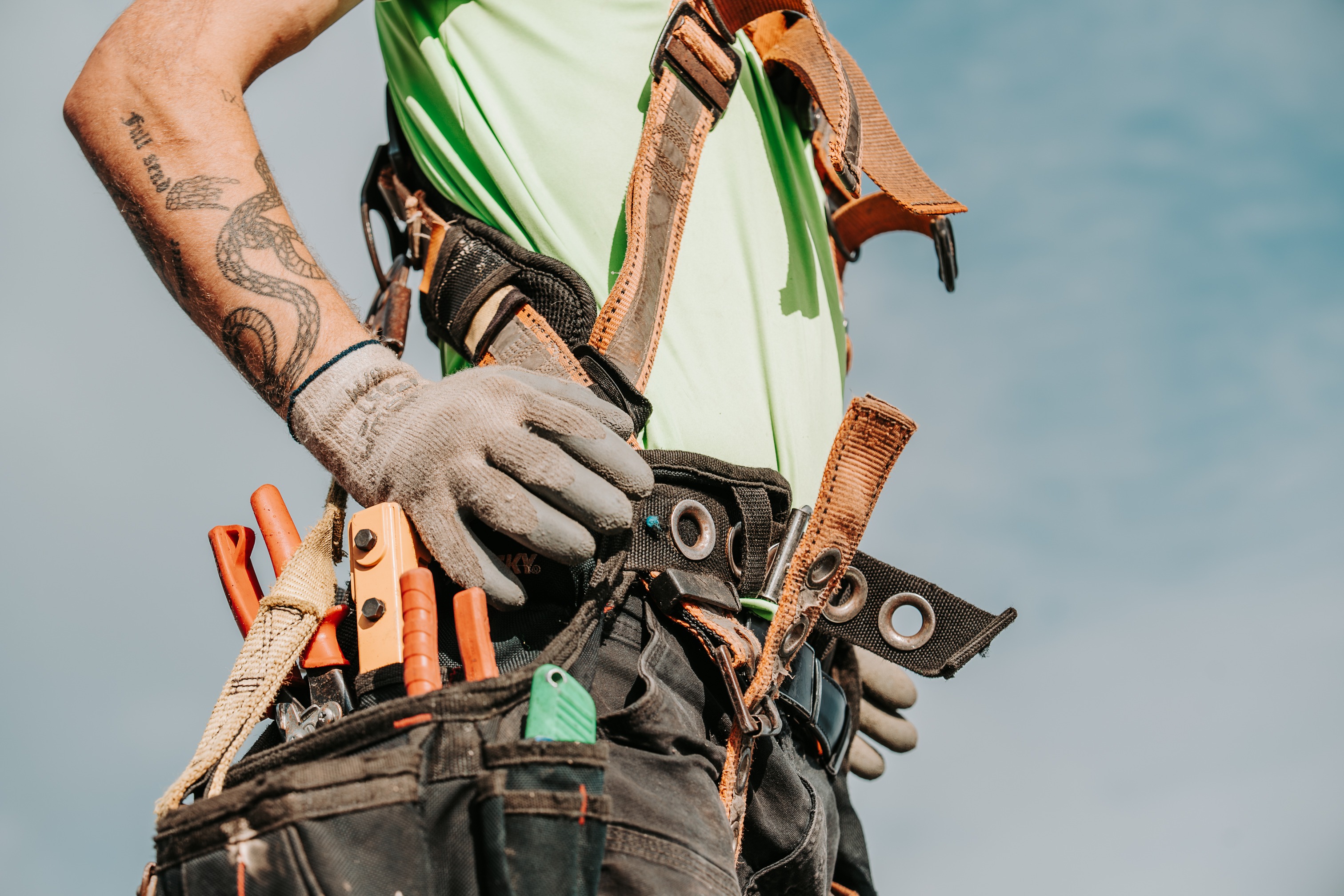 Roofing professional wearing a safety harness and tool belt while working on a residential roof. 