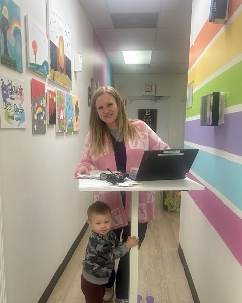 Kristin Morgan, APRN, with a child in the colorful clinic hallway at A+ Pediatrics in Irvine, KY.