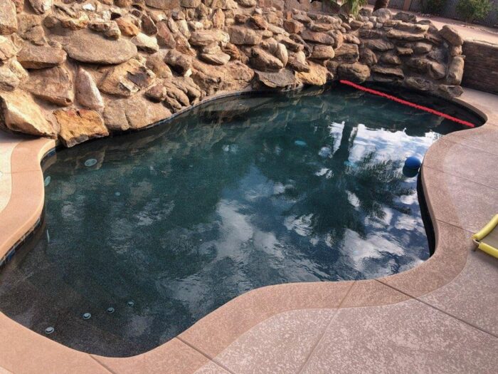 Finished freeform swimming pool featuring a dark interior finish and an extensive natural rock wall. 