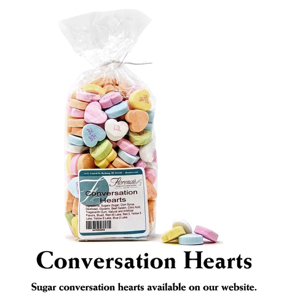 This photograph presents a bag of Florence's Exquisite Chocolates' "Conversation Hearts," likely from their Rexburg, Idaho location. The clear bag showcases the pastel-colored, heart-shaped candies with printed messages, tied with a simple white ribbon. The product label clearly identifies the contents and includes a barcode. Several loose conversation hearts are scattered beside the bag, revealing their pastel hues and small printed messages.