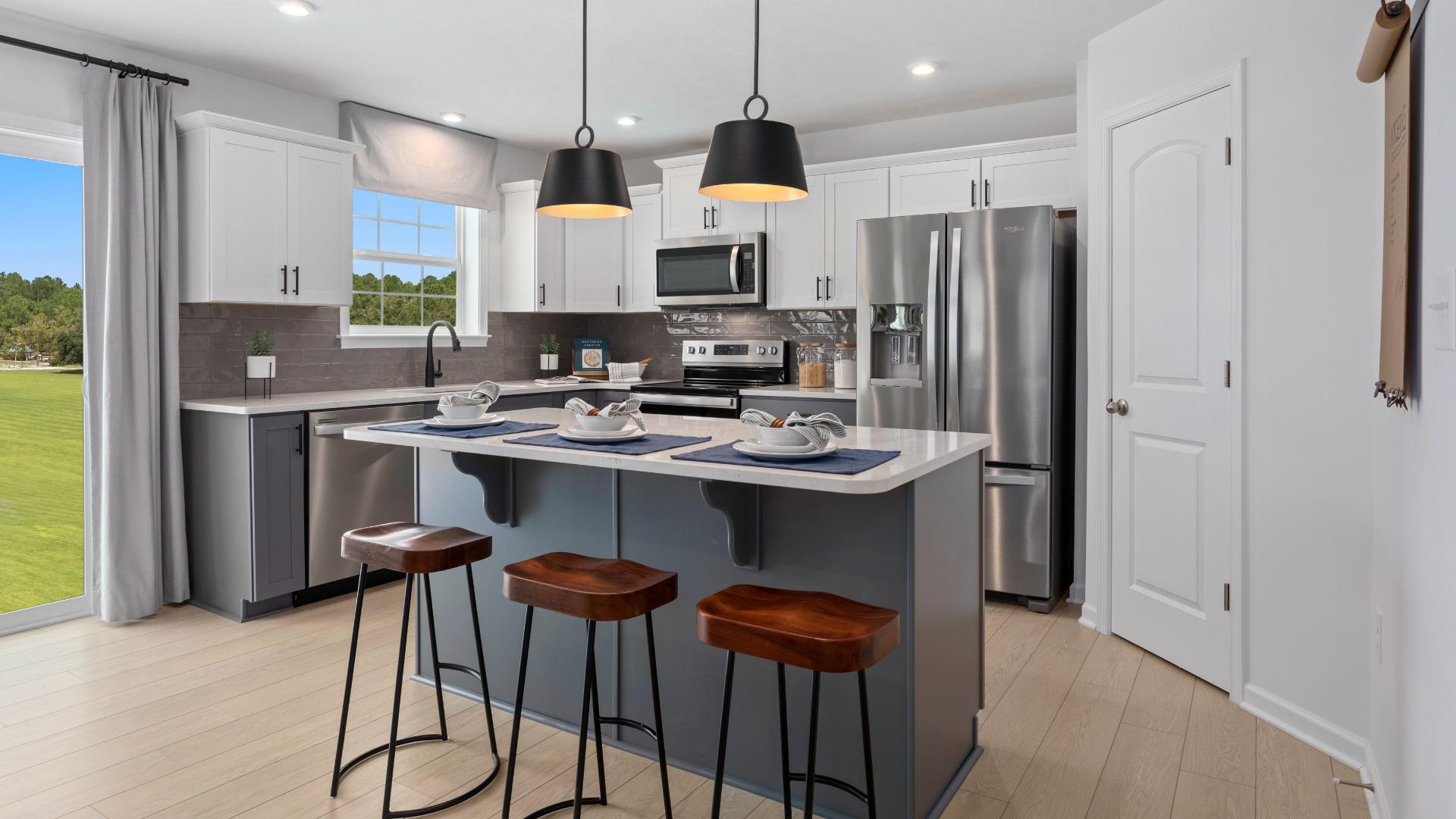 Kitchen with white cabinets, stainless steel appliances, gray island with 3 bar stools in DRB Homes Meadow Ponds Single Family Homes