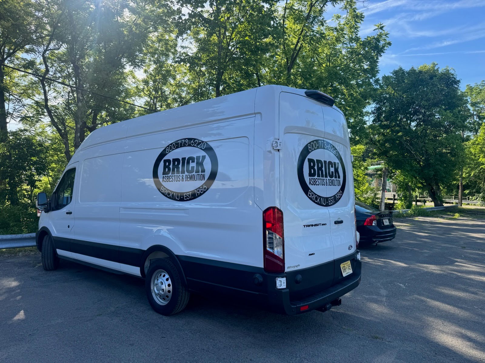 Brick Asbestos & Demolition van on-site at a residential property with a New Jersey licensed asbestos work sign displayed in the yard.