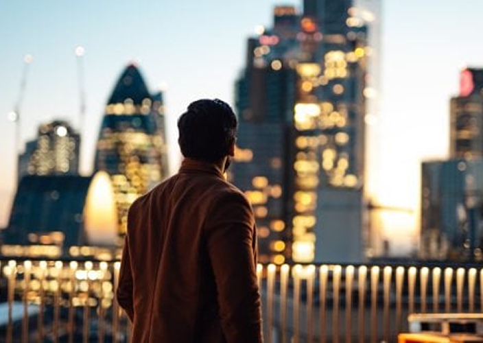 Un homme debout sur un balcon avec vue sur la ligne d'horizon de Londres la nuit.