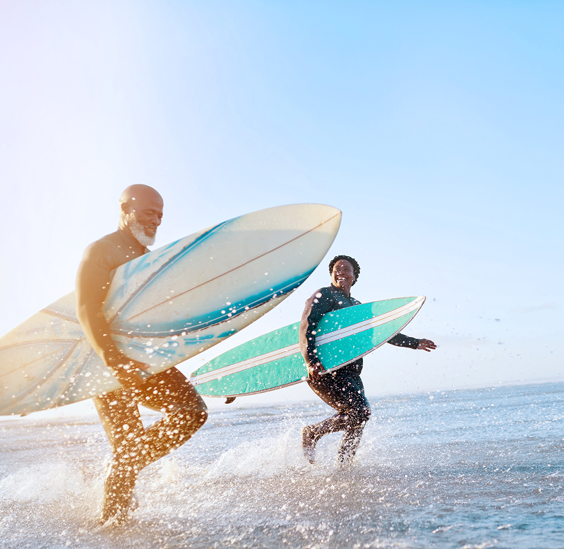 A husband and wife running into the ocean together with their surfboards.