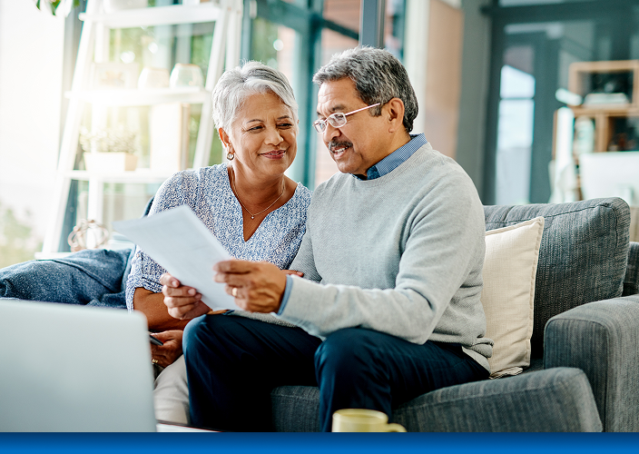 An elderly couple sitting together on their couch and reviewing a document.