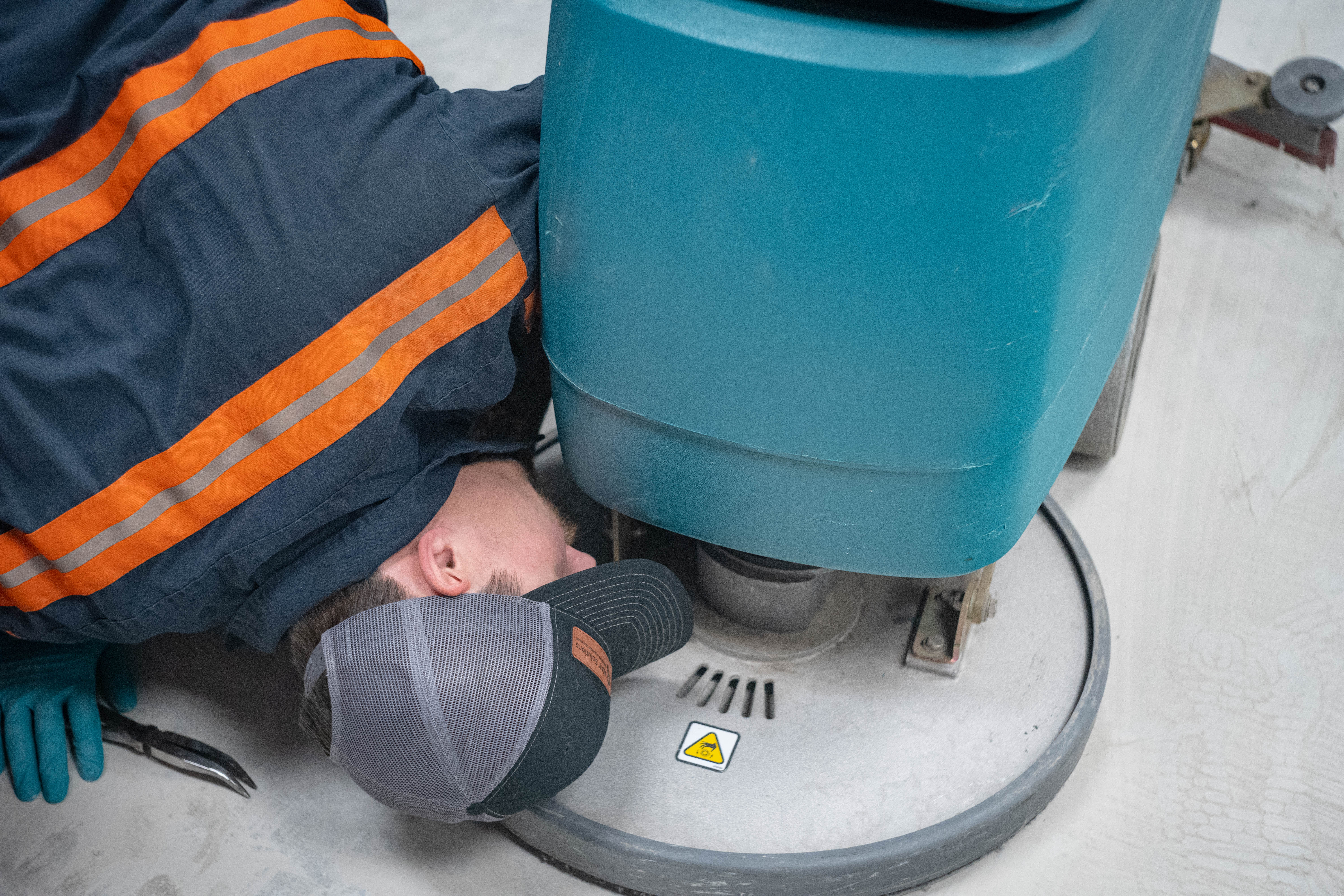 A dedicated WaySolutions technician, wearing a branded cap and high-visibility uniform with teal gloves, stands ready for service in a repair workshop. We provide top-tier commercial floor scrubber maintenance and repair services for B2B fleets throughout Layton, Utah.