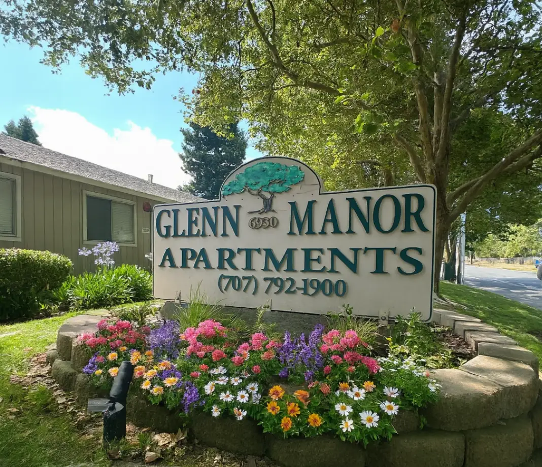 A sign for Glenn Manor Apartments is surrounded by flowers.
