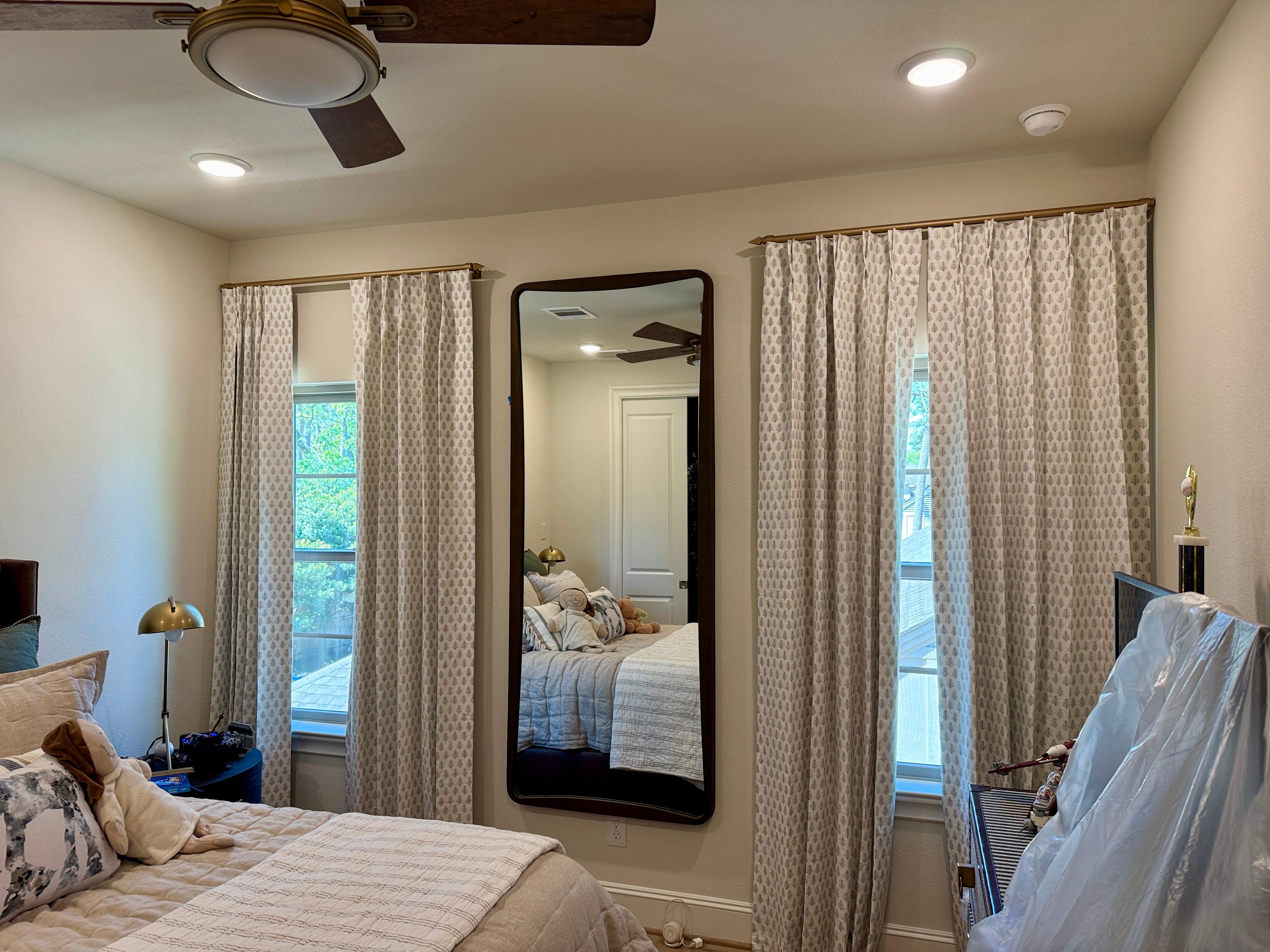 Full-length wall mirror installed between custom bedroom curtains in a residential home in Memorial Villages Houston, Texas.